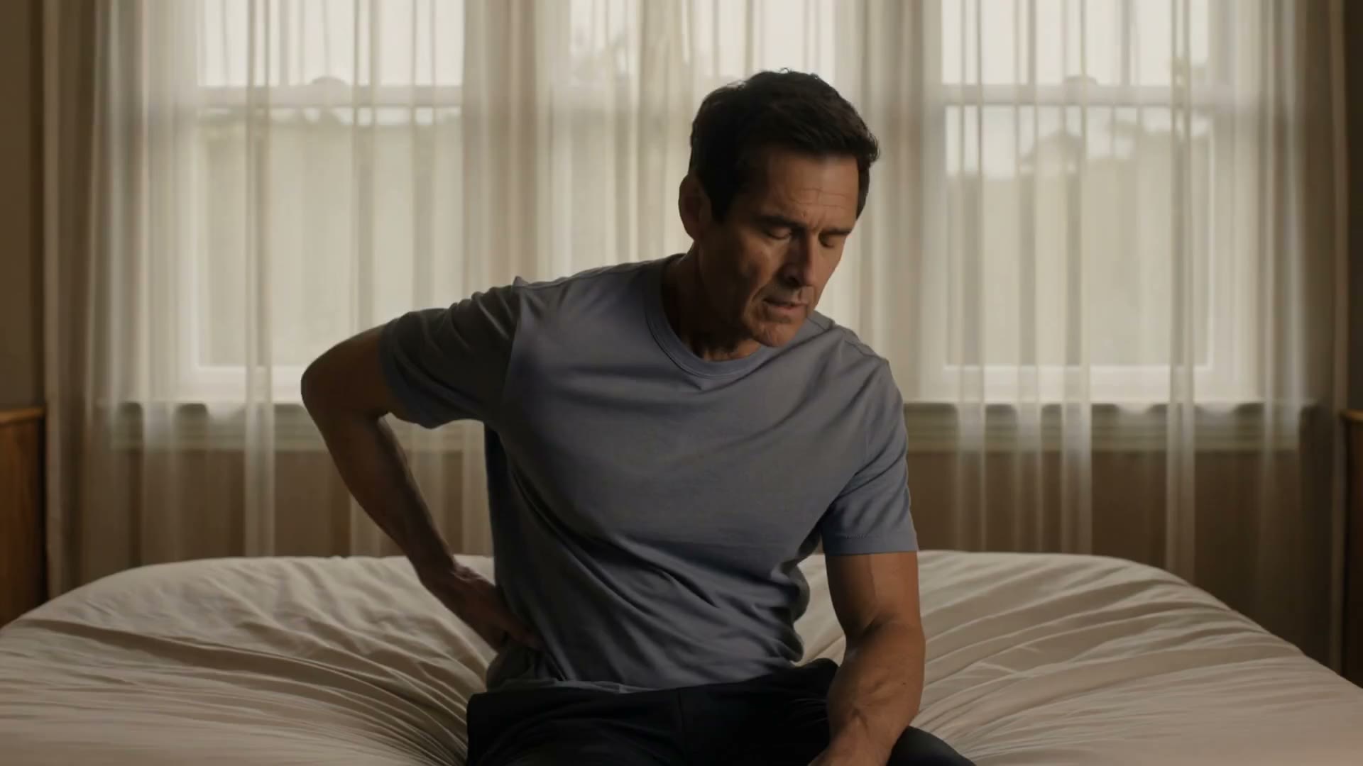 Man sitting on the edge of his bed, holding his lower back
